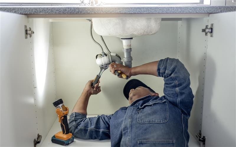 Plumber repairing pipes beneath a bathroom sink in Fort Myers