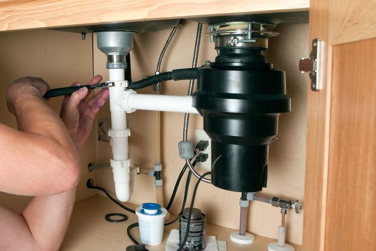 Plumber installing a garbage disposal beneath a kitchen sink in Fort Myers