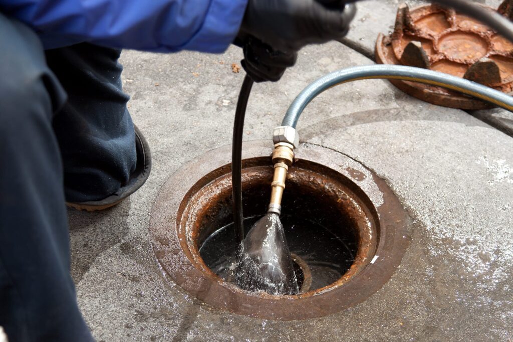 Plumber hydro jetting a sewer line through a manhole in Fort Myers