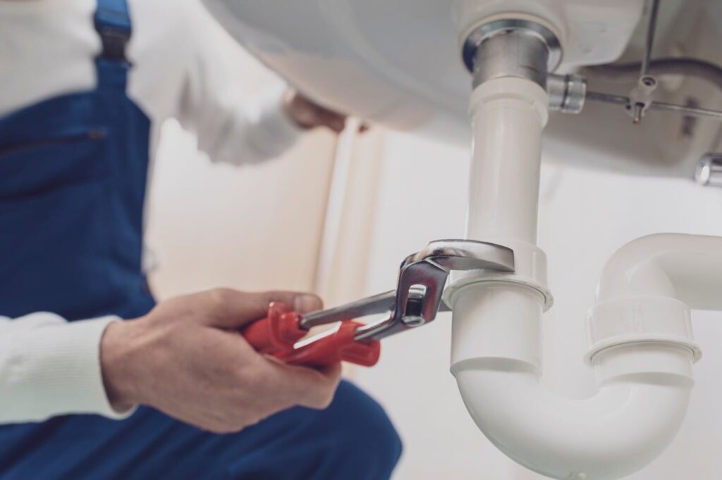 Plumber repairing a white drain pipe beneath a sink in Fort Myers