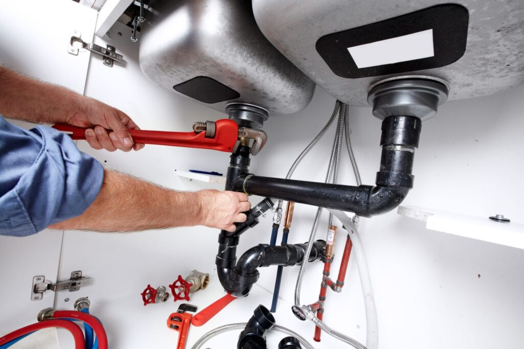 Plumber repairing drain pipes beneath a kitchen sink in Fort Myers